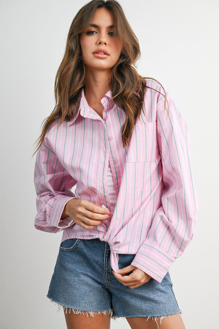 woman wearing a pink and white striped oversized button-up shirt knotted at the waist with denim shorts