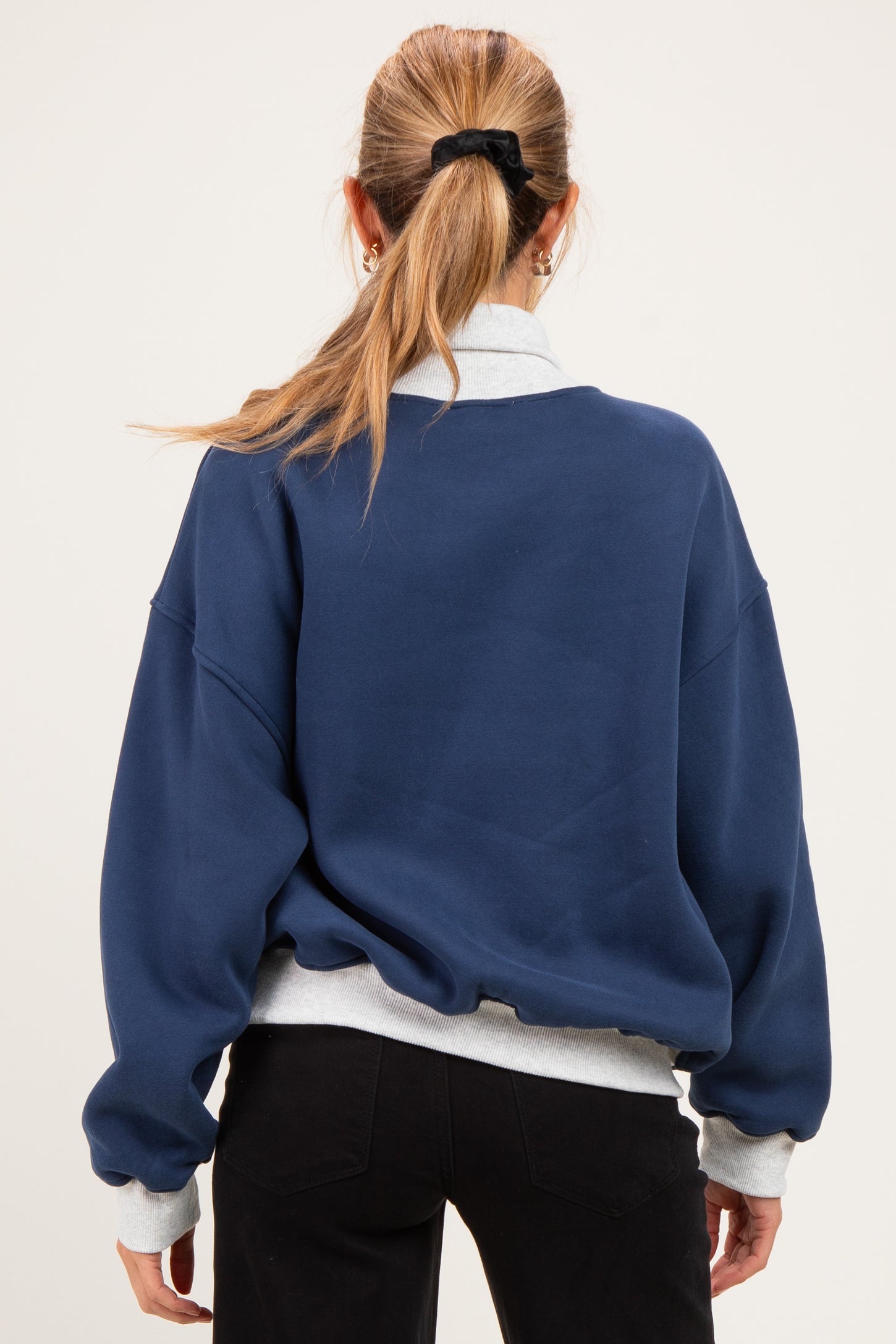 woman wearing a navy blue oversized maternity sweatshirt with a gray collar and back detail, styled casually