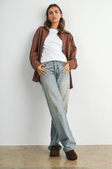 woman wearing a brown button-up shirt over a white t-shirt and light blue wide-leg jeans with brown slippers