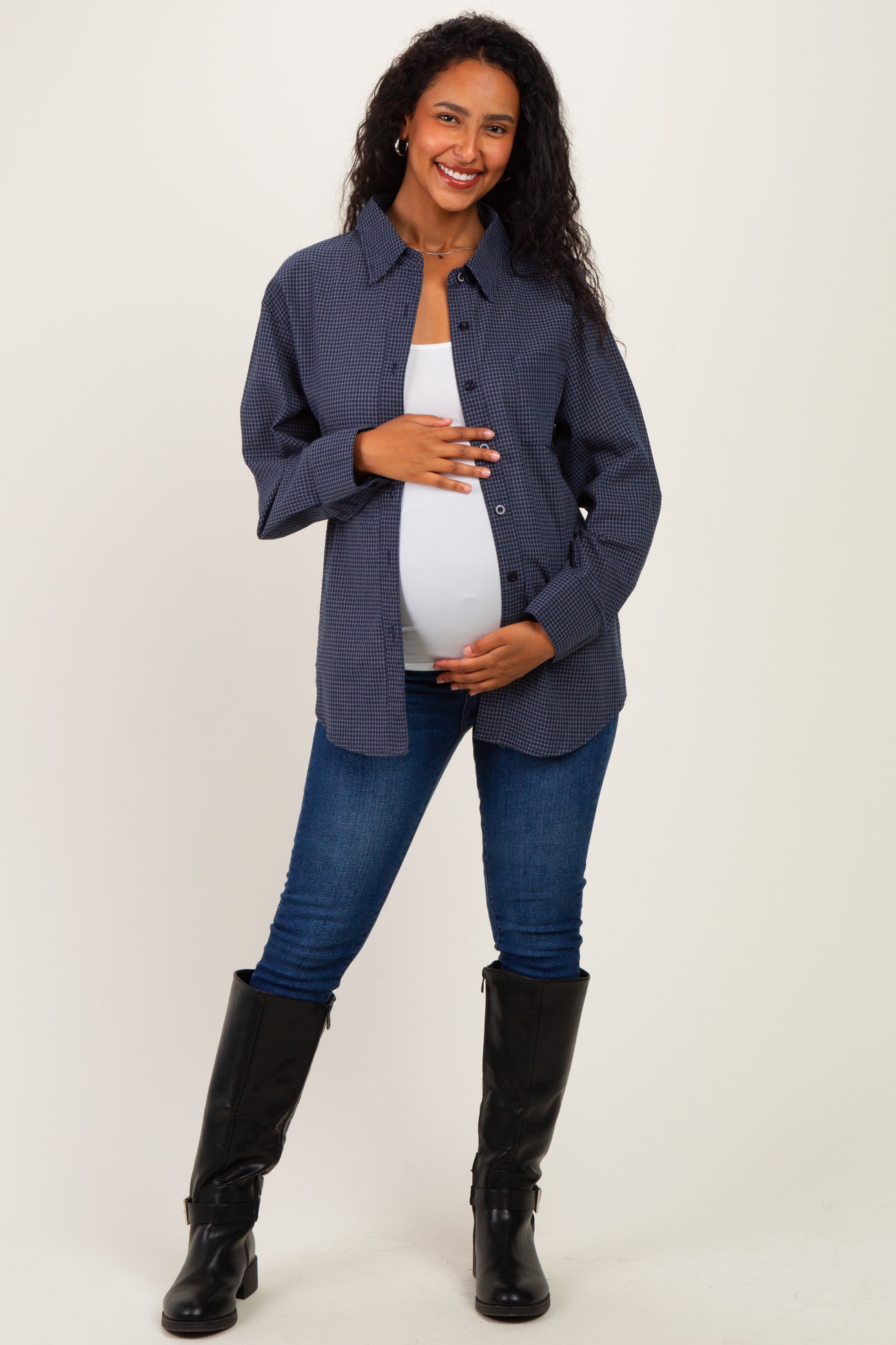 woman wearing a navy checkered maternity shirt and denim jeans, holding her baby bump