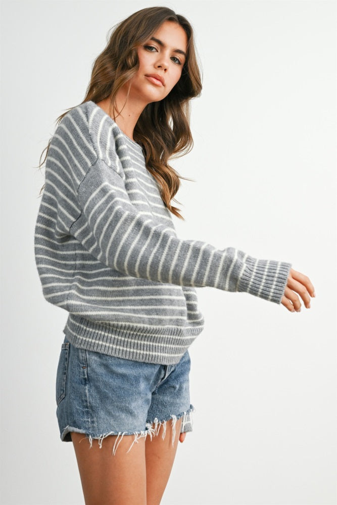 woman wearing a gray striped sweater and denim shorts, striking a side pose against a plain background