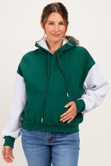 woman wearing a green and gray color-blocked maternity hoodie and holding her baby bump