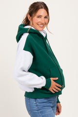 woman wearing a green and grey color-blocked maternity hoodie and holding her baby bump