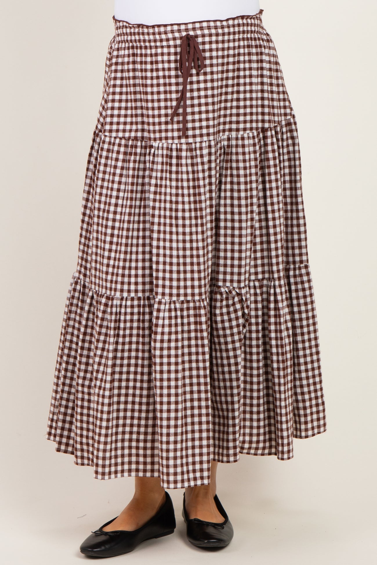 woman wearing a brown and white gingham patterned maternity maxi skirt with a drawstring waist and tiered design