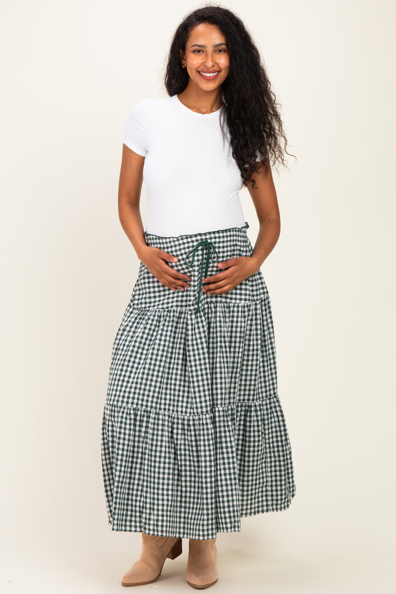 woman wearing a white short sleeve maternity top and a green and white gingham tiered maxi skirt, showing her baby bump
