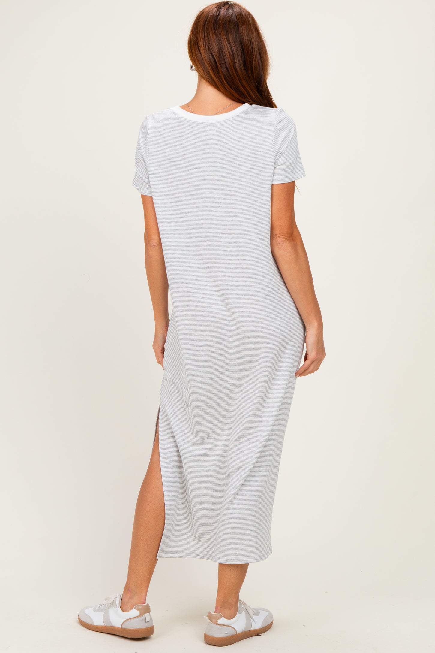 woman wearing a light gray short sleeve maxi dress with a side slit and white sneakers, viewed from the back