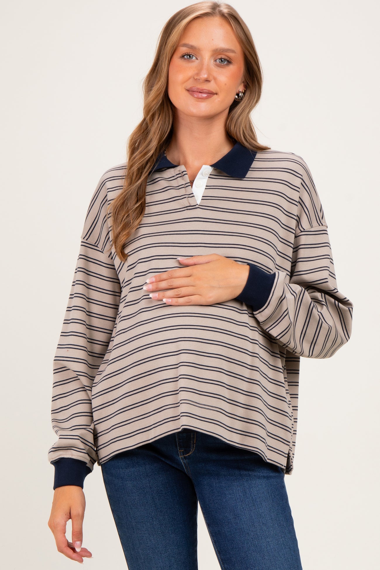 woman wearing a tan and navy striped maternity polo top and holding her baby bump