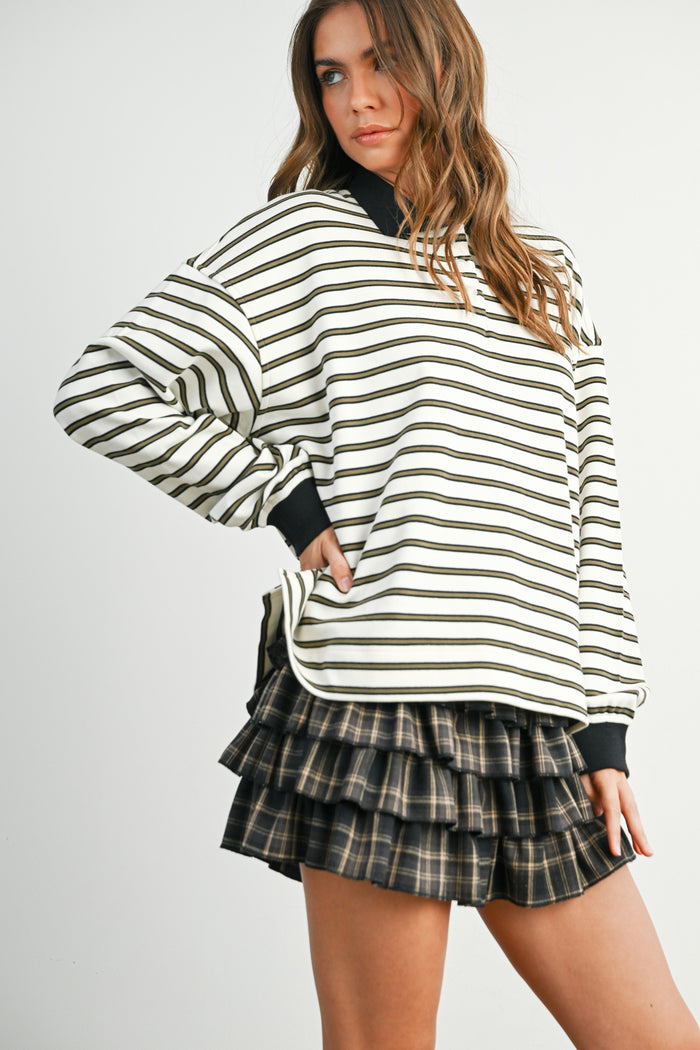 woman wearing a white and black striped oversized sweatshirt paired with a black and grey plaid ruffled mini skirt