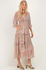 woman wearing a beige floral tiered maxi dress with puff sleeves and pockets, standing in strappy green heels
