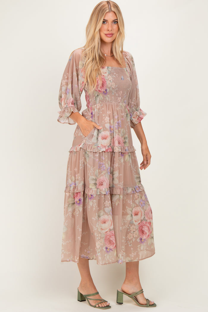 woman wearing a beige floral tiered maxi dress with puff sleeves and pockets, standing in strappy green heels