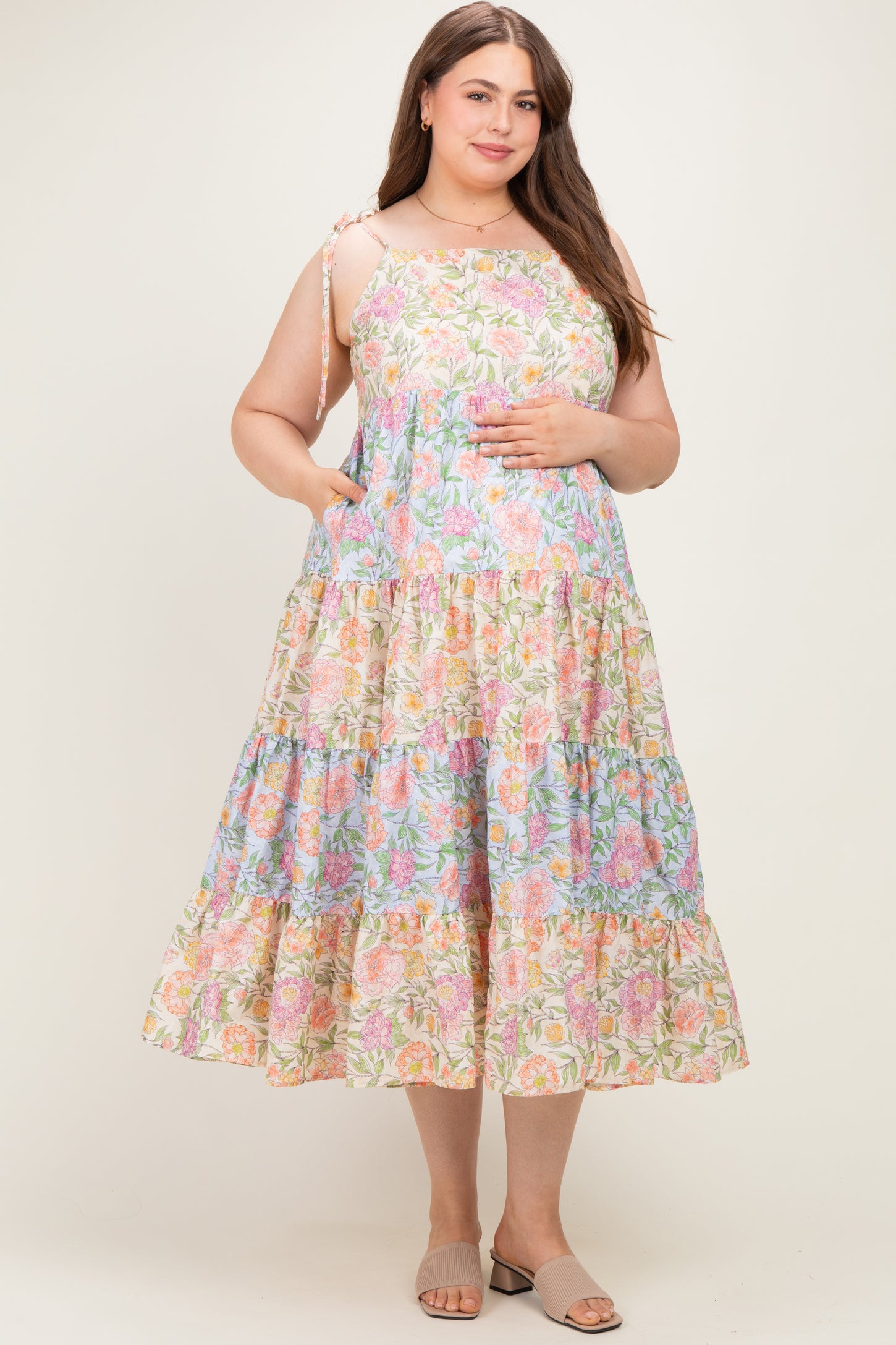 woman wearing a multicolored floral print maternity plus dress with tiered skirt and adjustable straps, showing her baby bump