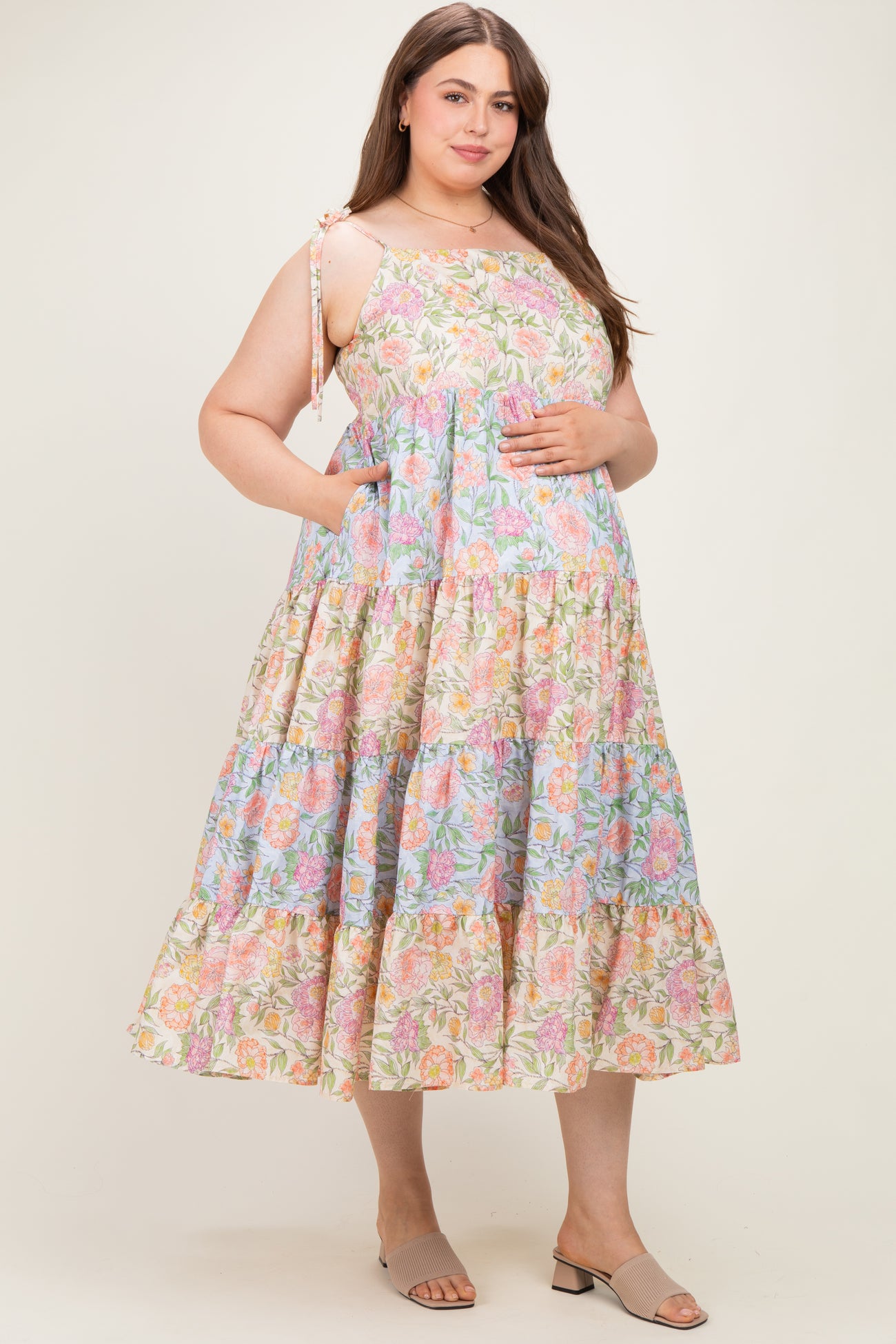 woman wearing a floral print maternity plus dress with adjustable straps and pockets, gently holding her baby bump