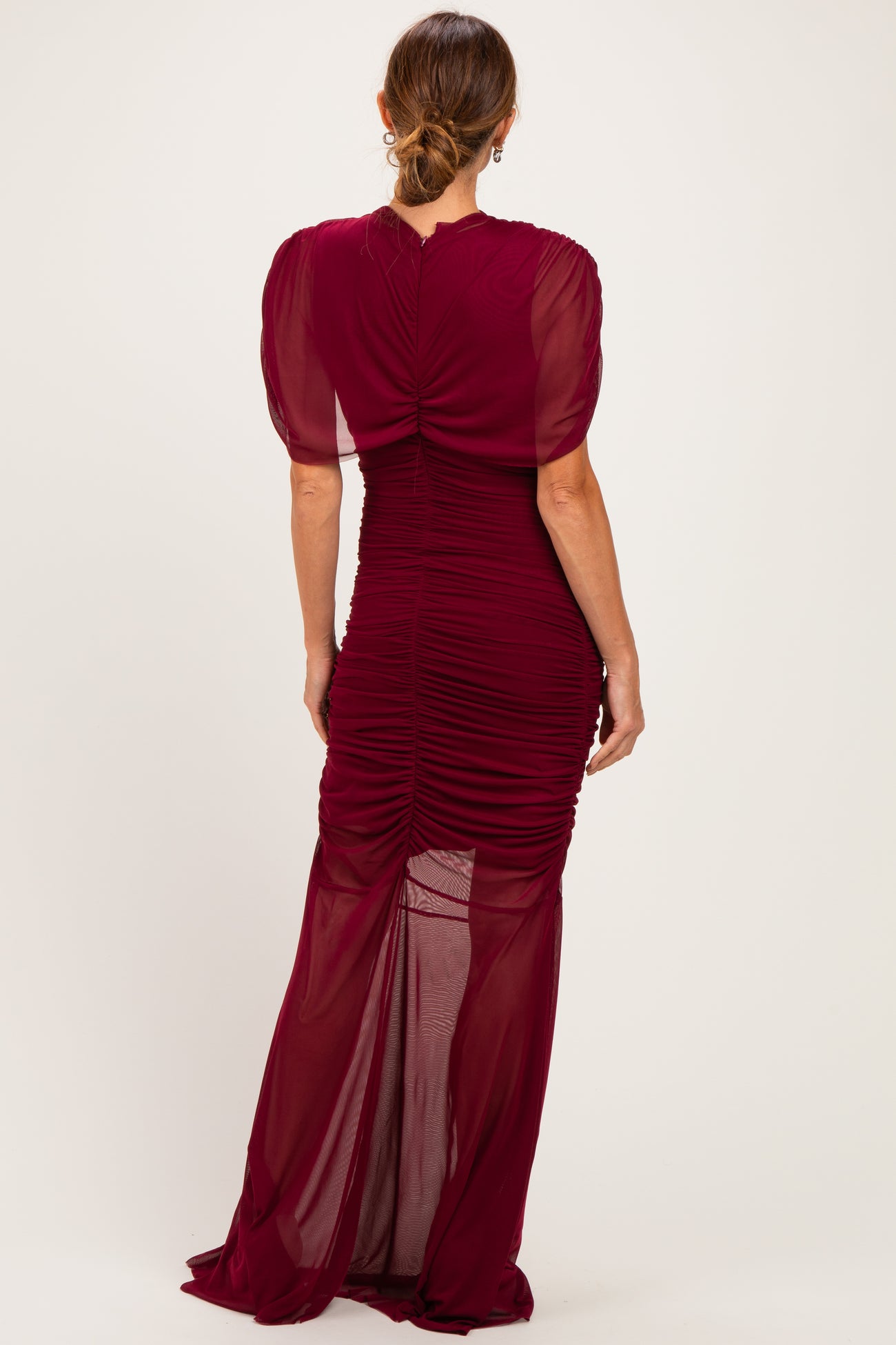 woman wearing a burgundy ruched evening gown with puff sleeves and a fitted silhouette, seen from the back