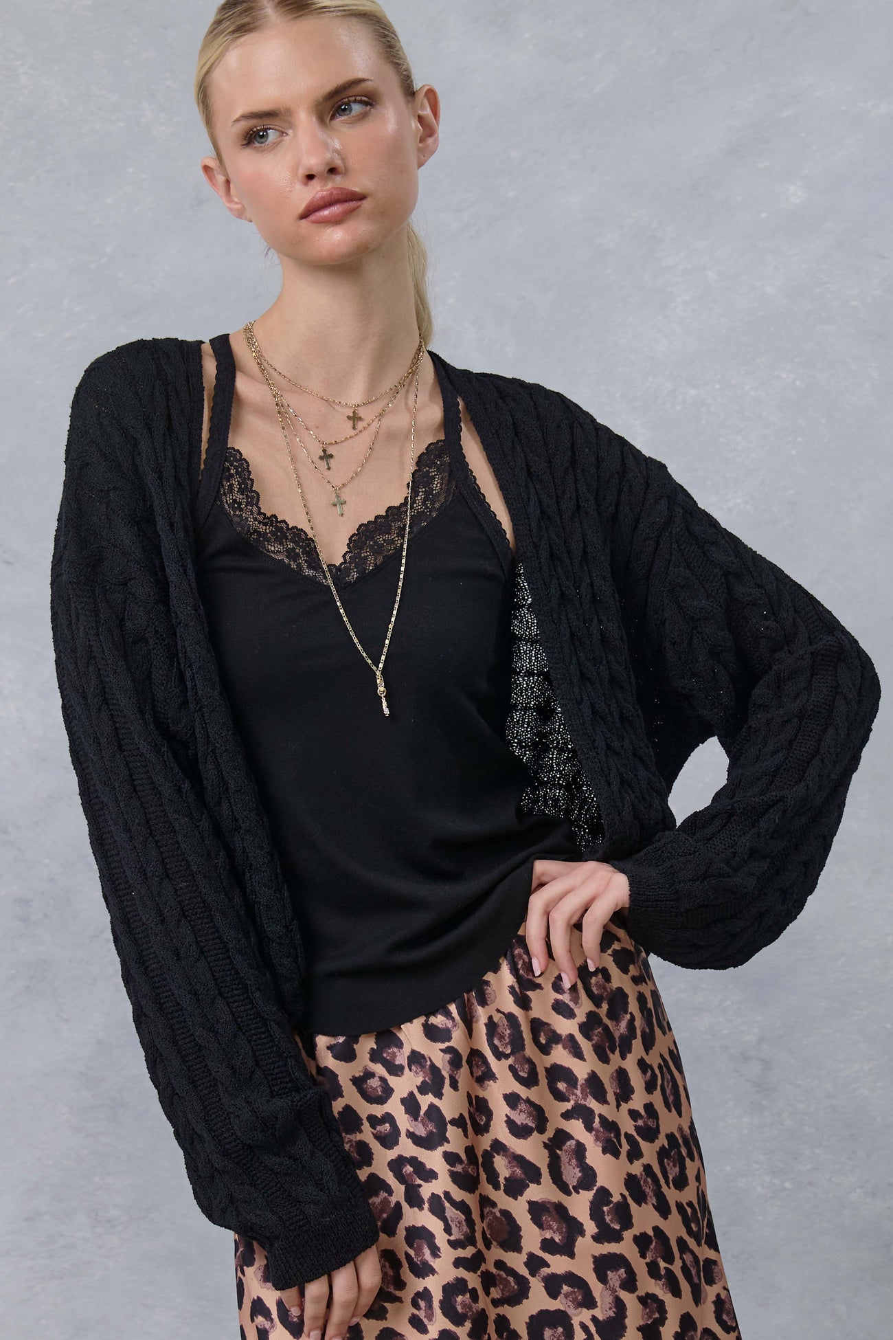 woman wearing a black cable knit cardigan over a black lace camisole and pink leopard print skirt