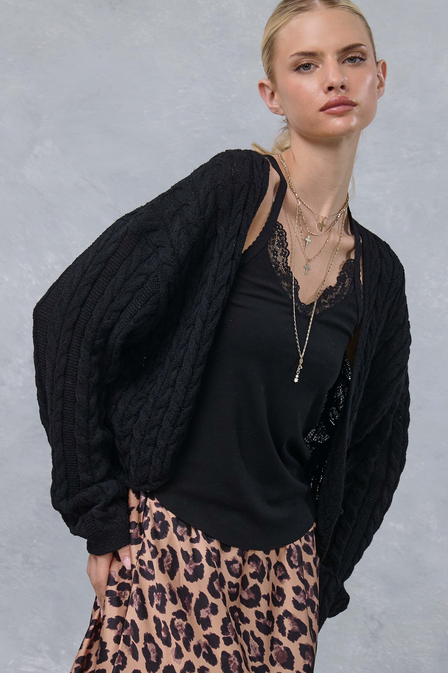 woman wearing a black cable knit cardigan over a black lace cami and a leopard print skirt, with layered necklaces