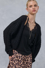 woman wearing a black cable knit cardigan over a black lace cami and a leopard print skirt, with layered necklaces