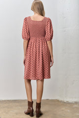 woman wearing a pink smocked dress with puff sleeves and black polka dots, viewed from the back