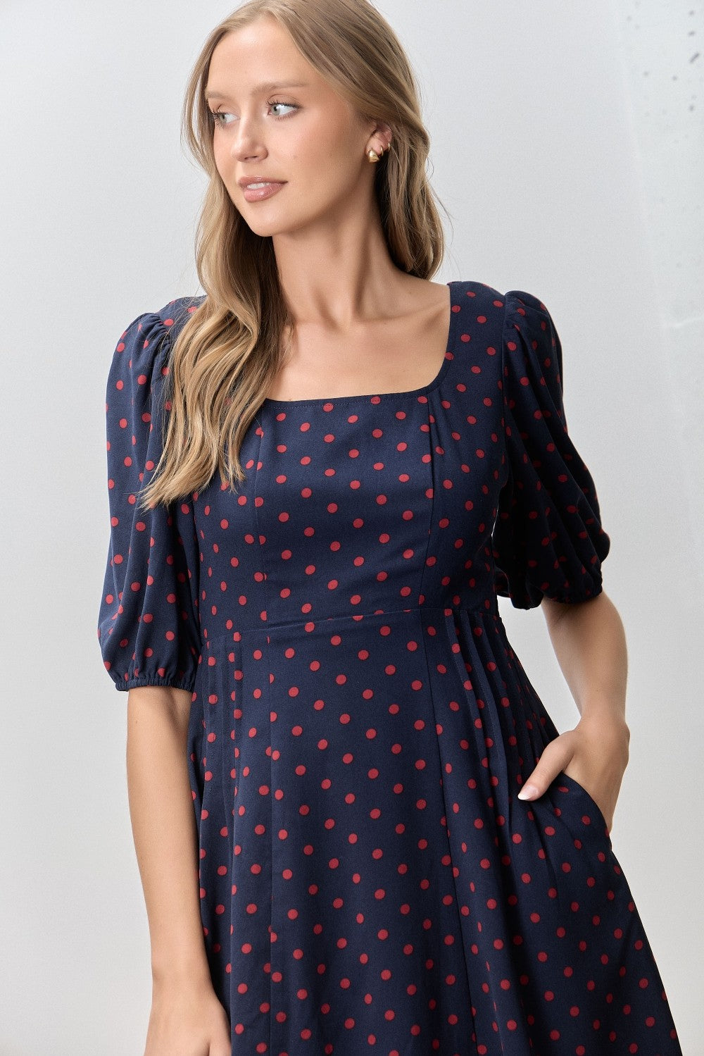 woman wearing a navy blue dress with red polka dots and puffed sleeves, featuring a square neckline and pockets