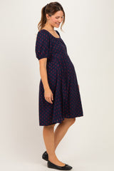 woman wearing a navy blue maternity dress with red polka dots and a fitted bodice, showcasing her baby bump
