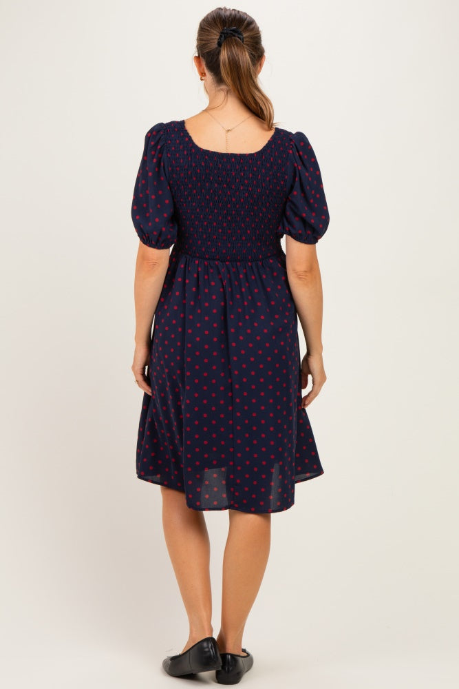 woman wearing a navy blue polka dot maternity dress with short puff sleeves and a smocked back design