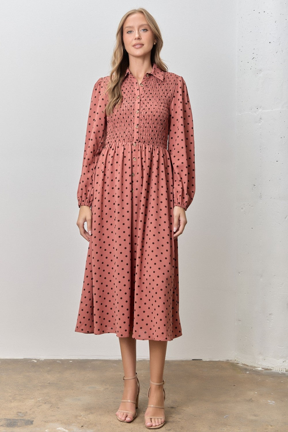 woman wearing a dusty rose button-up midi dress with polka dots and smocked waist, standing against a neutral background