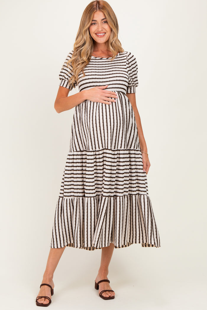 woman wearing a black and white striped maternity maxi dress with tiered ruffles and holding her baby bump