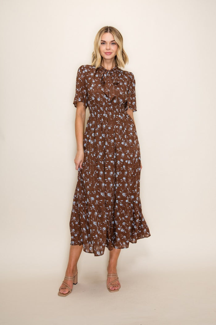 woman wearing a brown floral midi dress with short sleeves and a tie neck detail
