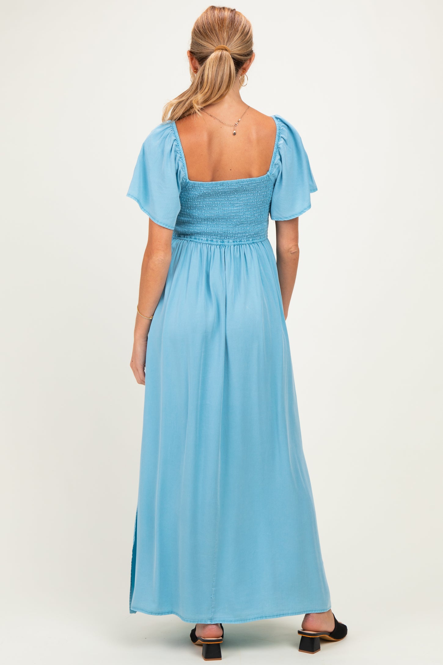 woman wearing a light blue maternity maxi dress with a smocked bodice and short puff sleeves, view from the back