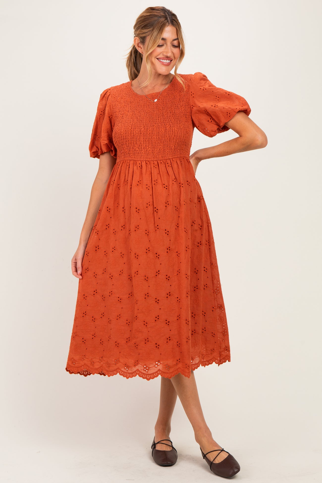 woman wearing an orange maternity dress with puff sleeves and floral embroidery, showing her baby bump