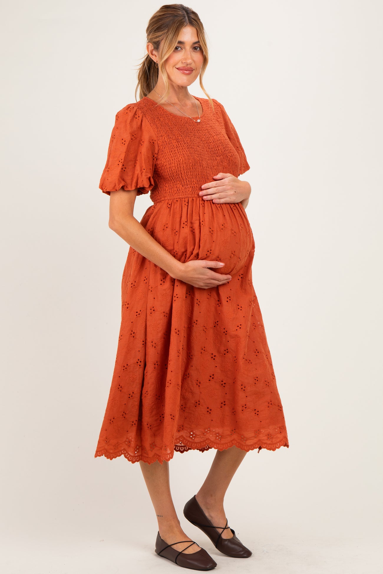 woman wearing an orange maternity dress with puff sleeves and a smocked bodice, holding her baby bump
