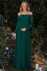 woman wearing a green lace off-shoulder maternity gown and cradling her baby bump in a garden setting