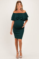 woman wearing a green off-the-shoulder maternity dress with ruffle details and holding her baby bump
