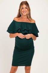 woman wearing a dark green off-the-shoulder maternity dress with ruffled sleeves and a visible baby bump
