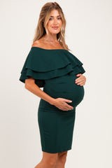 woman wearing a dark green off-the-shoulder maternity dress with ruffles and holding her baby bump