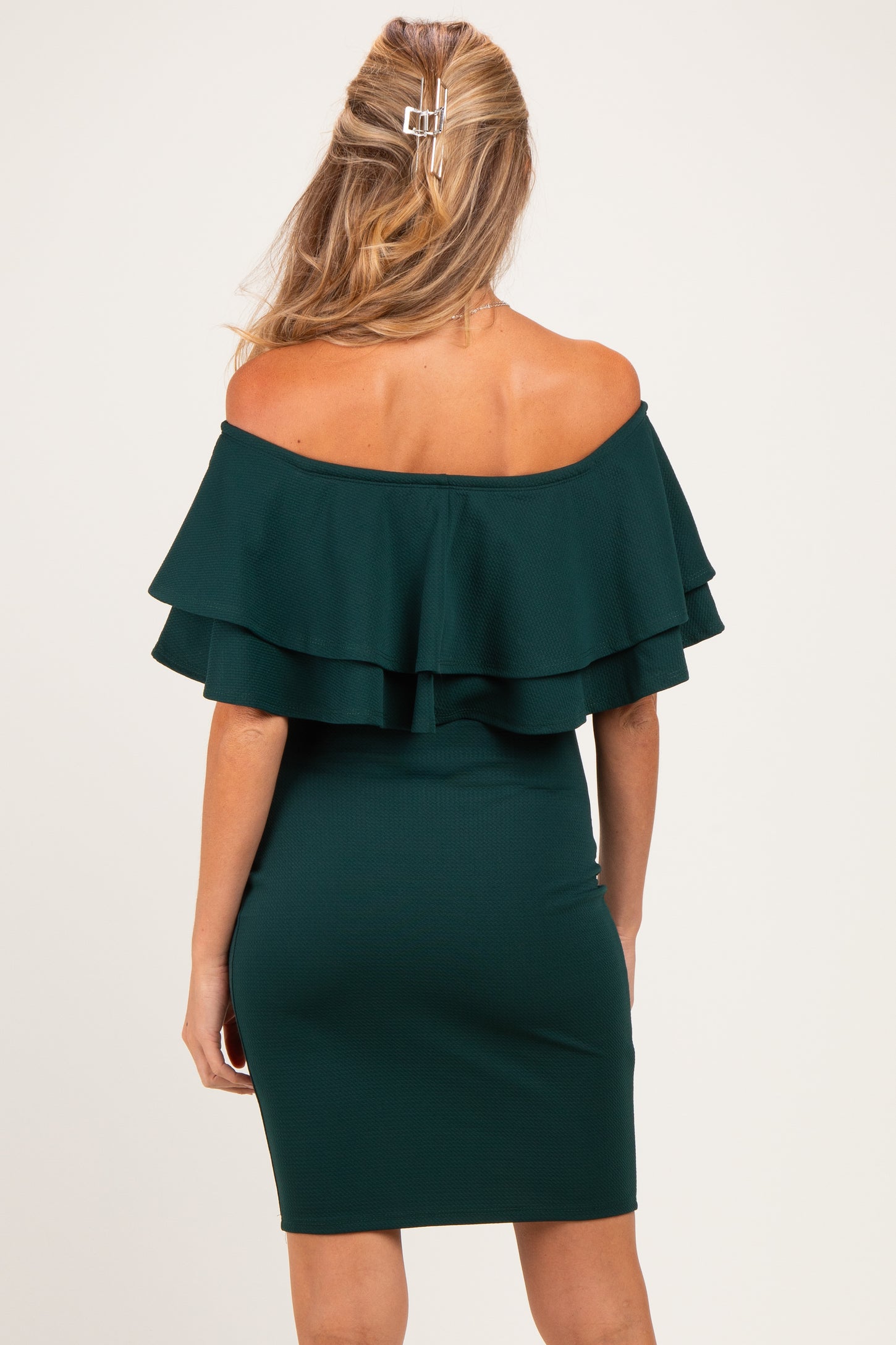 woman wearing a dark green off-the-shoulder maternity dress with ruffled sleeves and a fitted silhouette