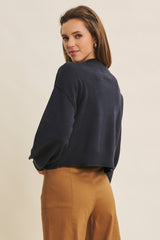 woman wearing a navy cropped sweater with long sleeves and a relaxed fit, paired with tan high-waisted trousers