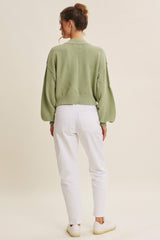 woman wearing a green oversized knit sweater and white high-waisted jeans, seen from the back