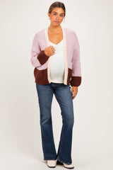 woman wearing a pastel pink and brown maternity cardigan over a white top, paired with flared jeans and showing her baby bump