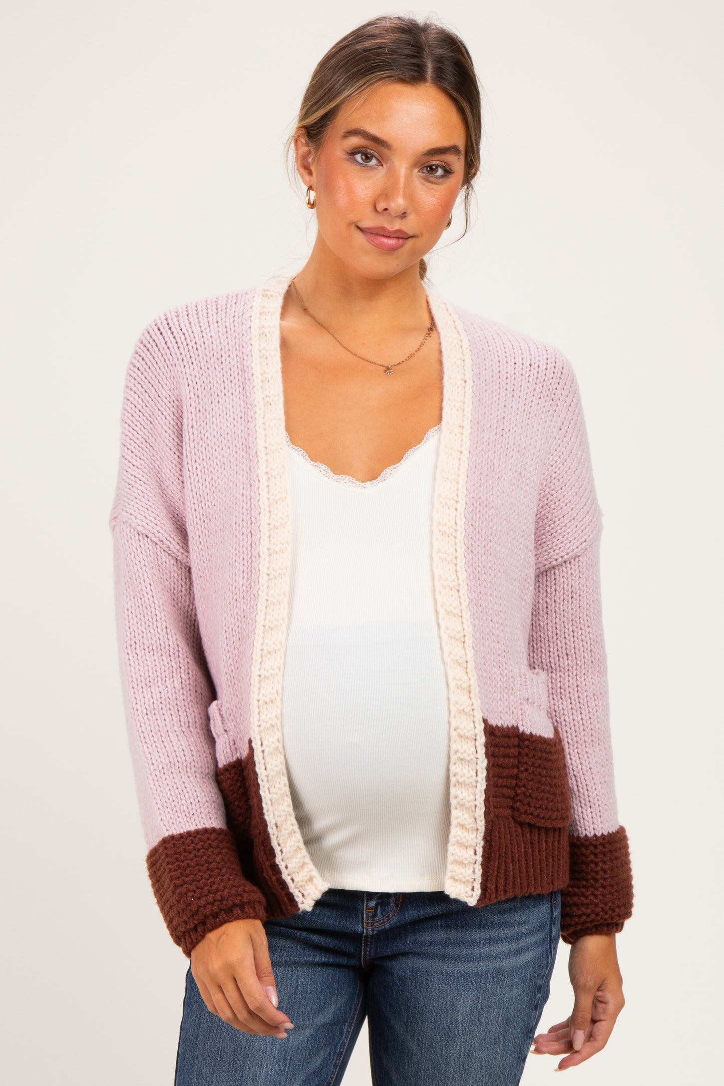 woman wearing a light pink and brown color block maternity cardigan over a white top and showing her baby bump