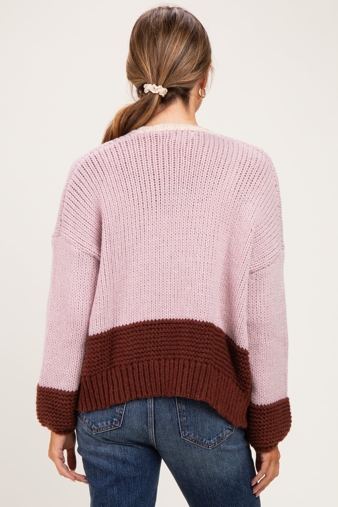 woman wearing a pink and brown striped maternity sweater with a relaxed fit, seen from the back