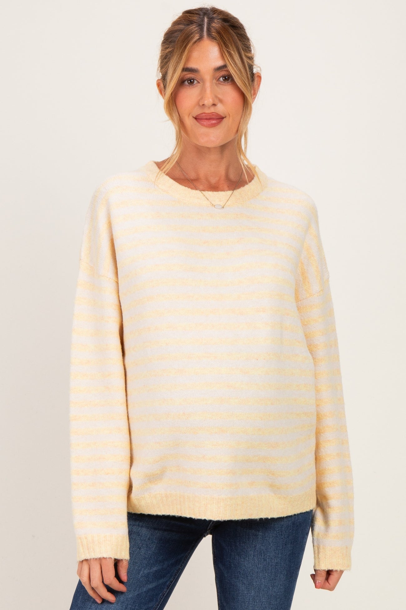 woman wearing a yellow and white striped maternity sweater with loose fit and long sleeves over denim jeans