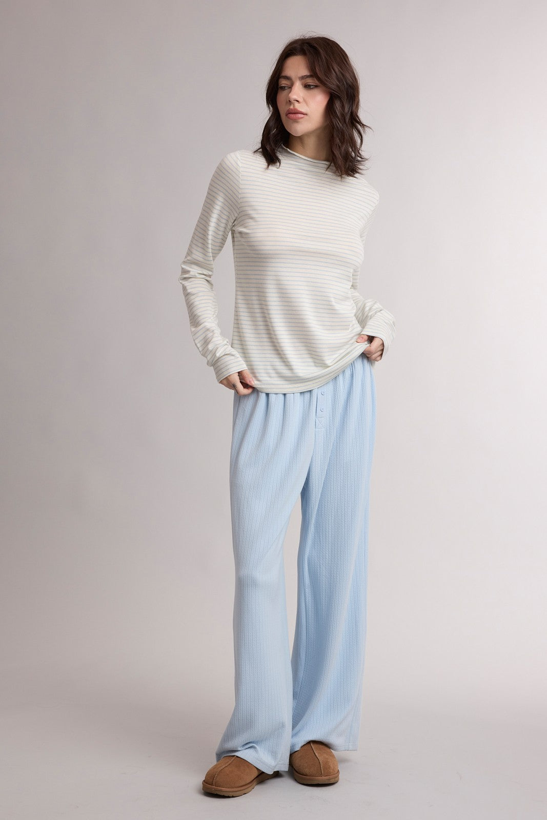woman wearing a light striped long sleeve top and blue wide-leg pants, standing with hands in pockets