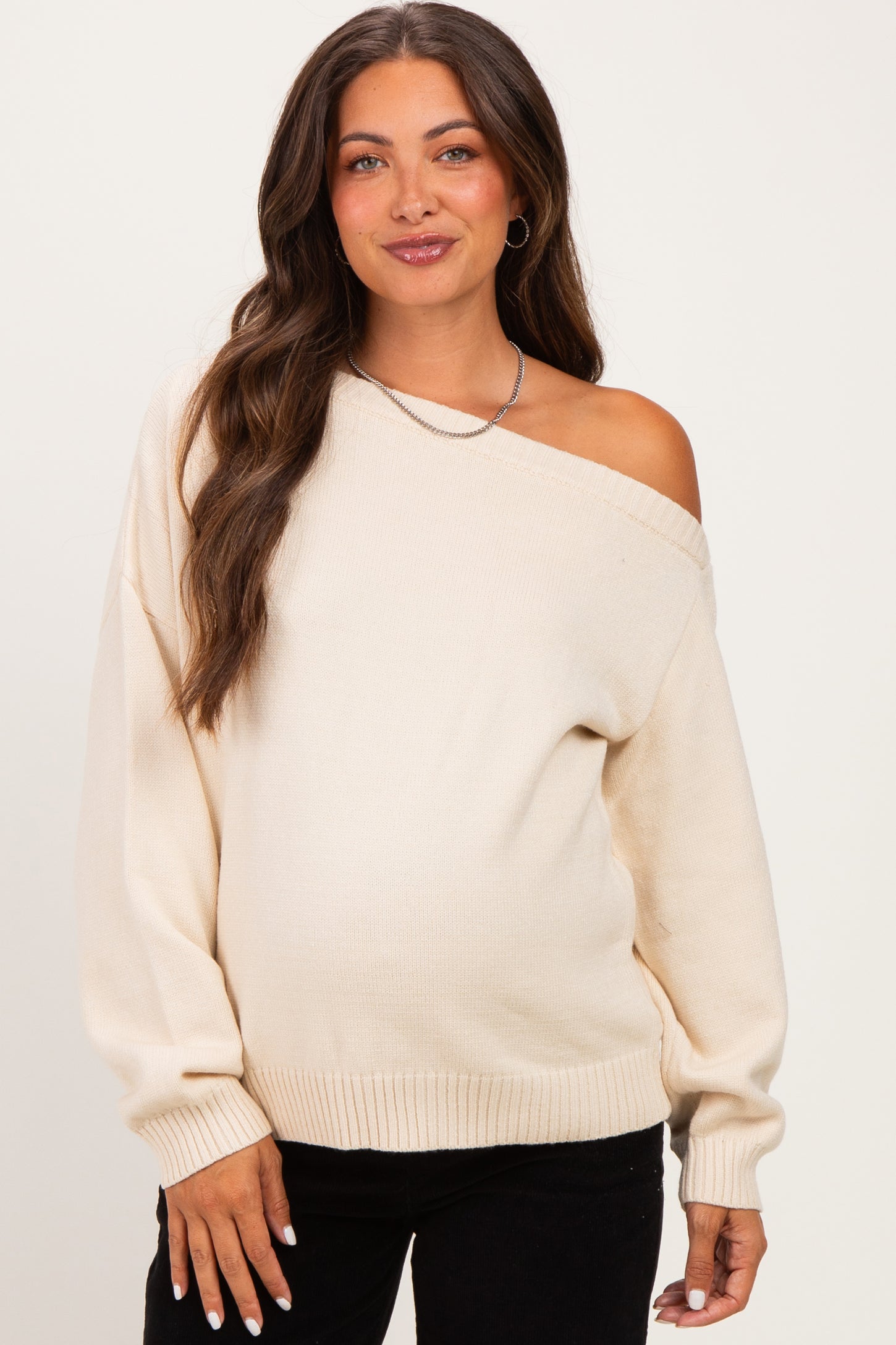 woman wearing a cream off-the-shoulder maternity sweater and showing her baby bump