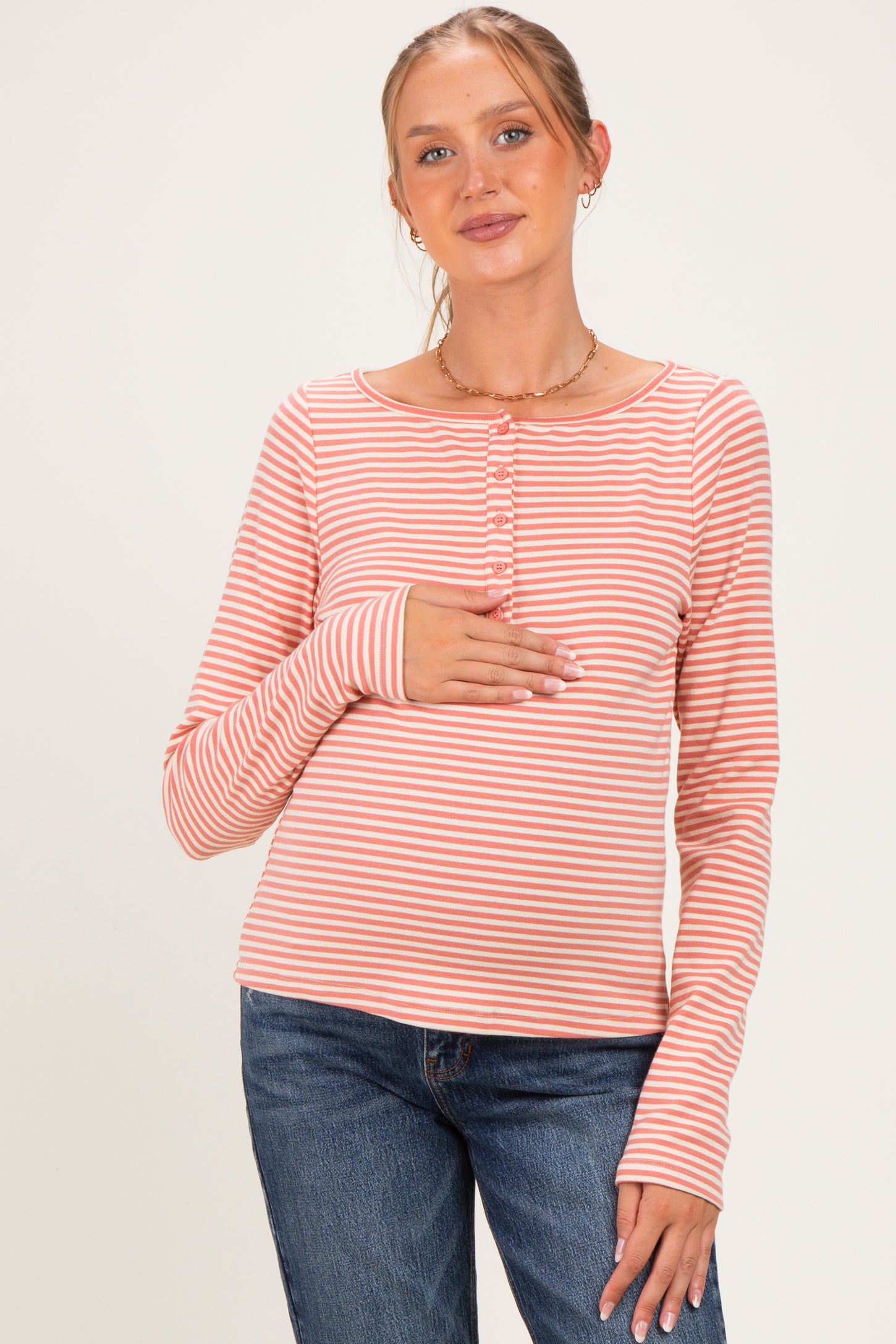woman wearing a striped long sleeve maternity top and gently holding her baby bump