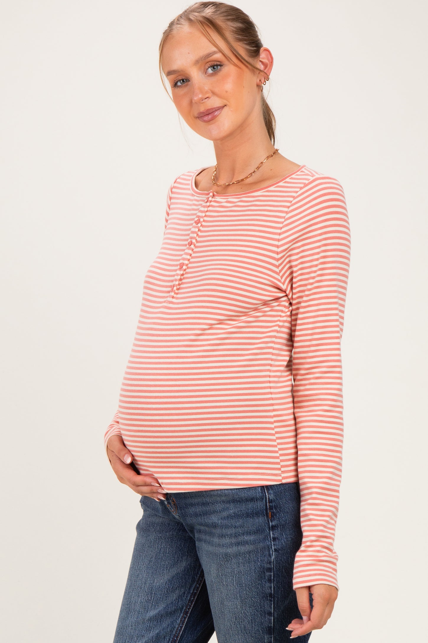 woman wearing a pink and white striped long sleeve maternity top and holding her baby bump