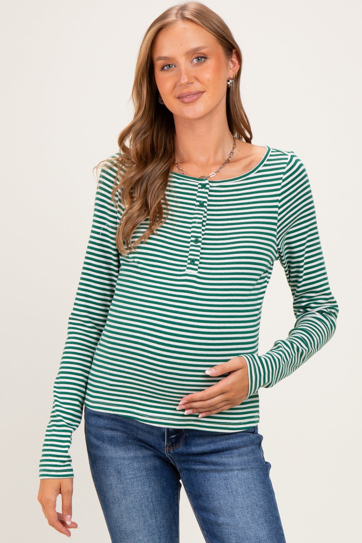 woman wearing a green and white striped long sleeve maternity top and holding her baby bump
