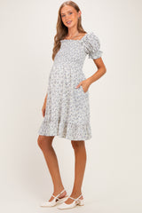 woman wearing a blue floral maternity dress with puff sleeves and ruffled hem, holding pockets, showing her baby bump