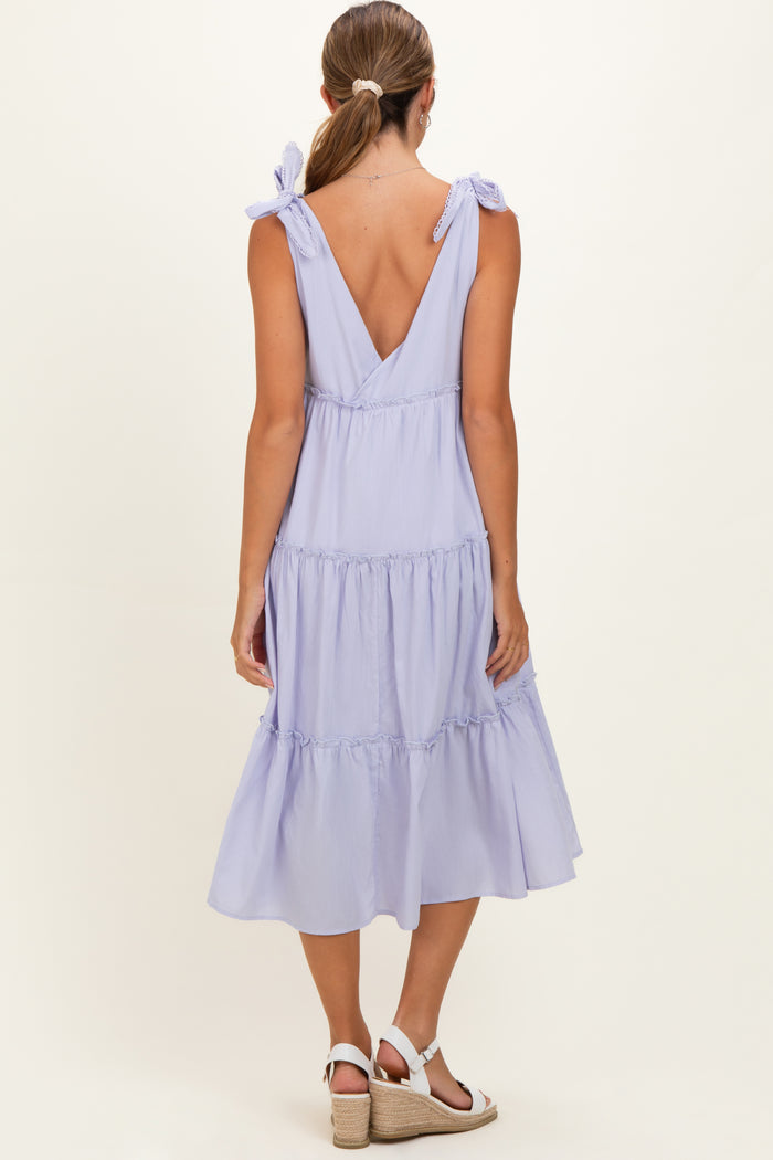 woman wearing a light purple maternity dress with tie straps and a tiered skirt, showing the back view