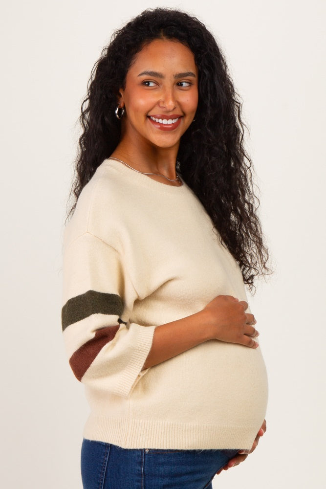 woman wearing a cream maternity sweater with striped sleeves and holding her baby bump