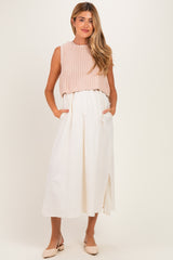 woman wearing a light pink knitted crop top and a white midi skirt with pockets, styled as maternity wear